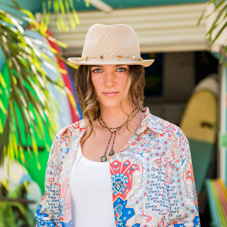 Woman exploring a coastal town, accessorized with the Wallaroo Waverly Short Brim Trilby Sun Hat, offering stylish sun protection with a breathable, natural fiber design, Natural