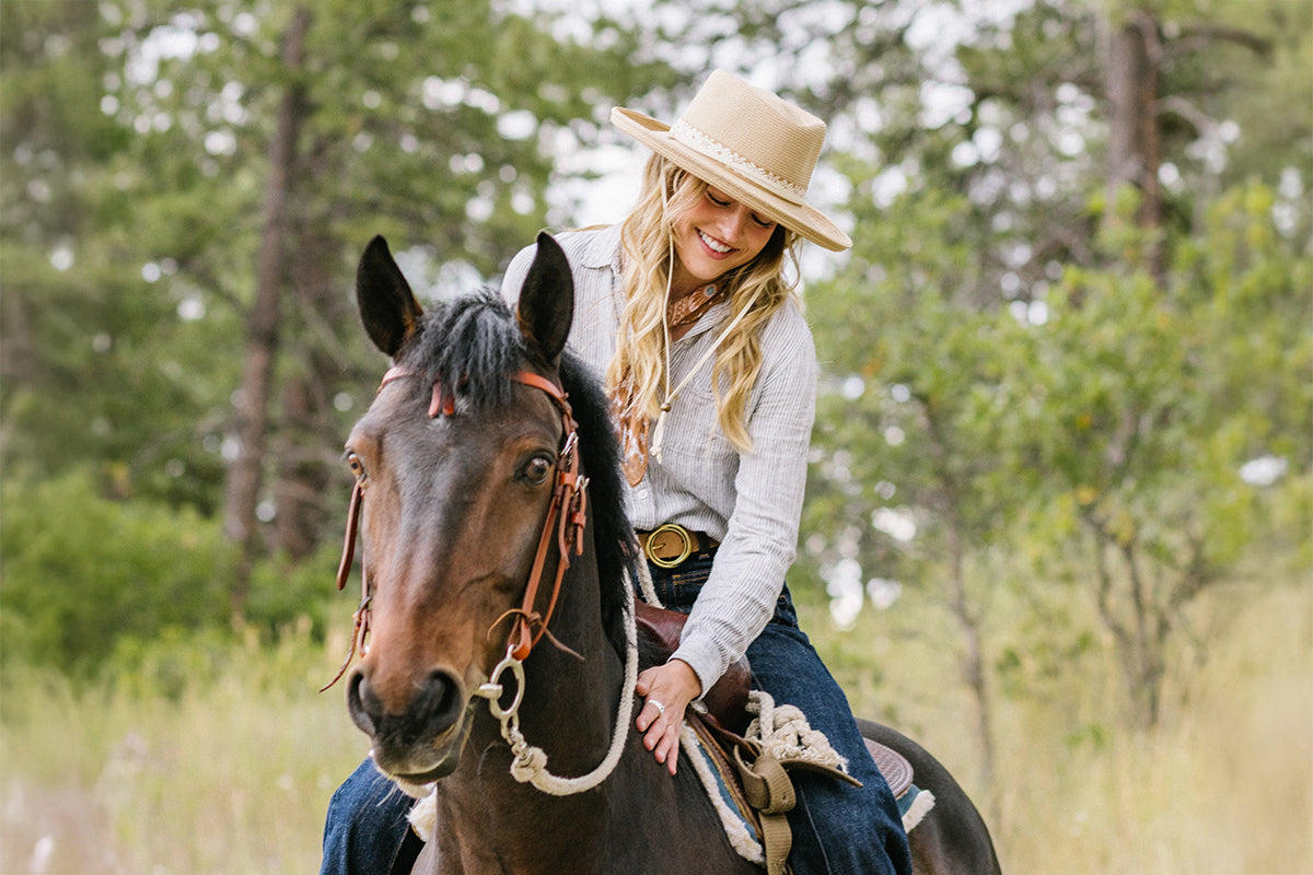 Woman wearing the Stevie fedora riding a horse in a forested area